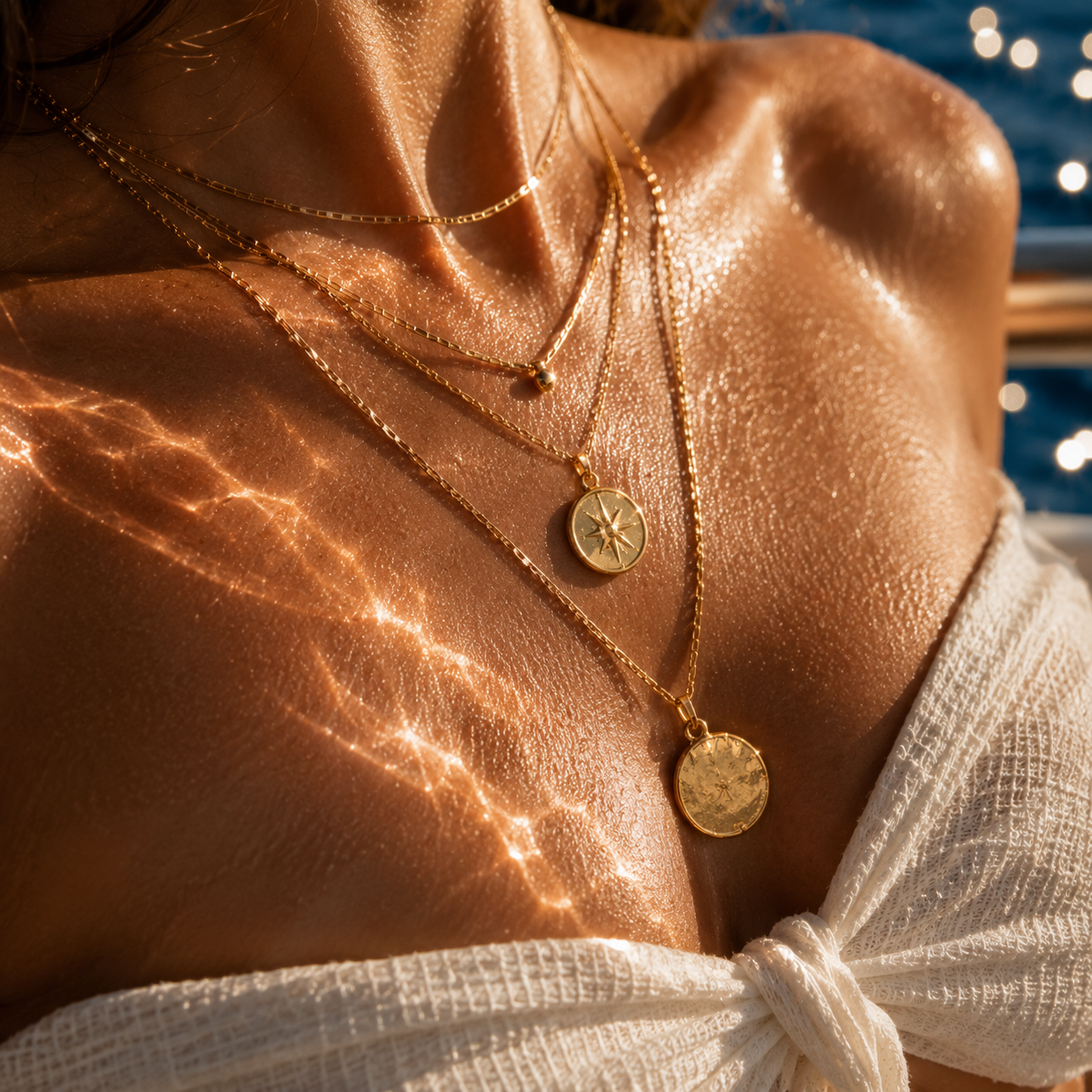 Close-up of a person wearing gold necklaces with circular pendants on a sunlit background.